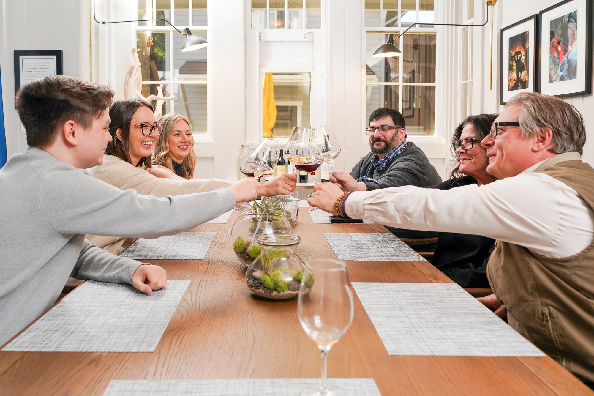 Group of people sitting around a dining table with wine glasses, engaged in conversation.